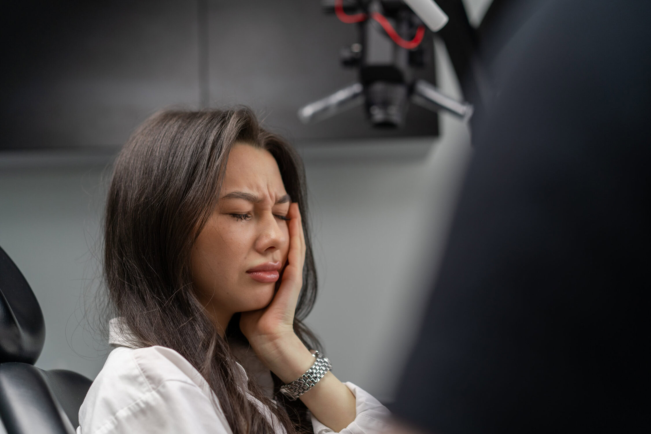 Woman holding her jaw in pain while sitting in a dental chair during an emergency dentist visit