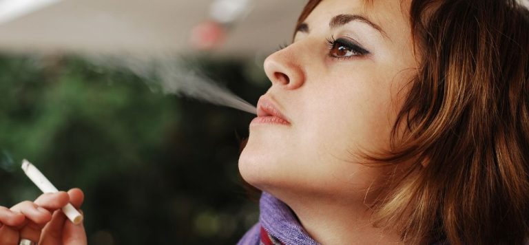 A woman smoking a cigarette and blowing out smoke.