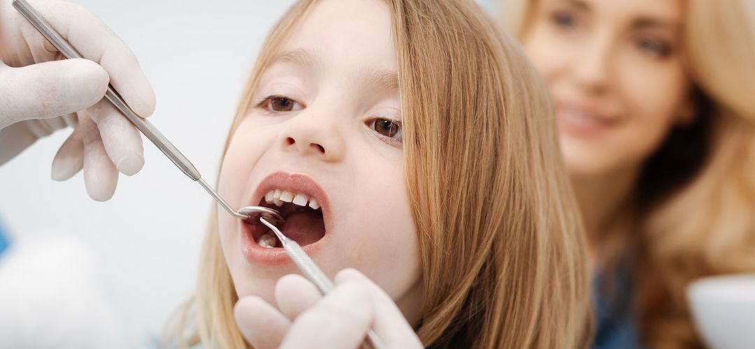 A child getting checked by a dentist with a parent.