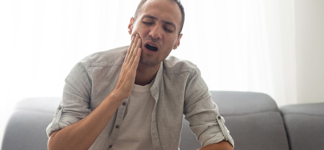 Man holding his hand to the side of his face as if he has tooth pain.