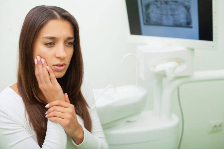 Young woman holding her jaw in pain at a dental clinic while an X-ray is visible in the background during an emergency dentistry visit in San Ramon